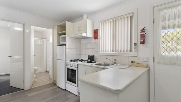 A compact kitchen with white cabinetry, a built-in oven, a stove, and a sink.