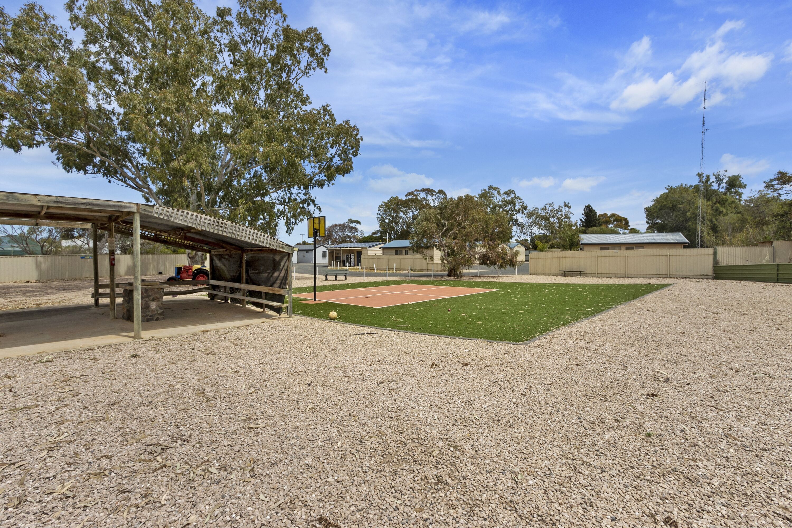 A covered seating area with a bench, a small table, and a tennis court in the background.