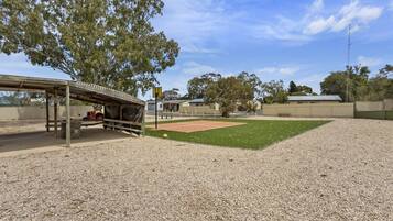A covered seating area with a bench, a small table, and a tennis court in the background.