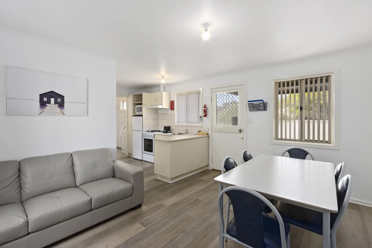A modern kitchen with a central island, a dining area with a white table and blue chairs, and a beige sofa.
