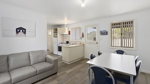 A modern kitchen with a central island, a dining area with a white table and blue chairs, and a beige sofa.