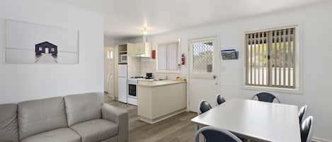 A modern kitchen with a central island, a dining area with a white table and blue chairs, and a beige sofa.