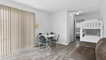 A modern, well-lit room with a dining area, a bunk bed, and a wooden floor.