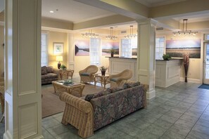 A spacious living room with a sofa, chairs, and a coffee table. There is a kitchen area with a counter and a window with blinds.