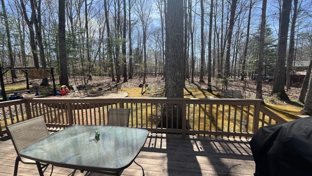 A deck with a glass table and chairs, overlooking a forested area with a playground and a barbecue grill. - LU Commencement Rental - Easy 15 minute drive to LU campus. (Forest)