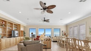 A spacious living room with a sofa, chairs, a dining table, and ceiling fans. - Beach Castle, West. 8BR. Sleeps 27. Large Pool! Great decks,, Beachfront. Value! (Gulf Shores)