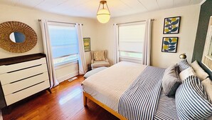 Een slaapkamer met een bed, een stoel, een dressoir en een raam met gordijnen.