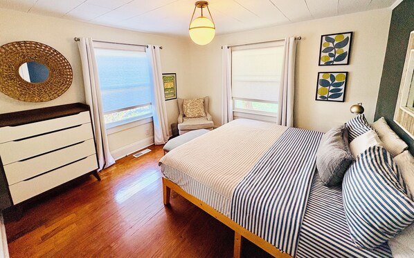 A bedroom with a bed, a chair, a dresser, and a window with curtains.