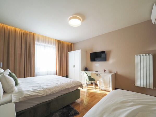 A modern hotel room with two beds, a desk, a television, and a radiator.