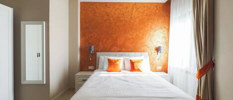A modern hotel room with a large bed, two bedside tables, and a wall-mounted light fixture.
