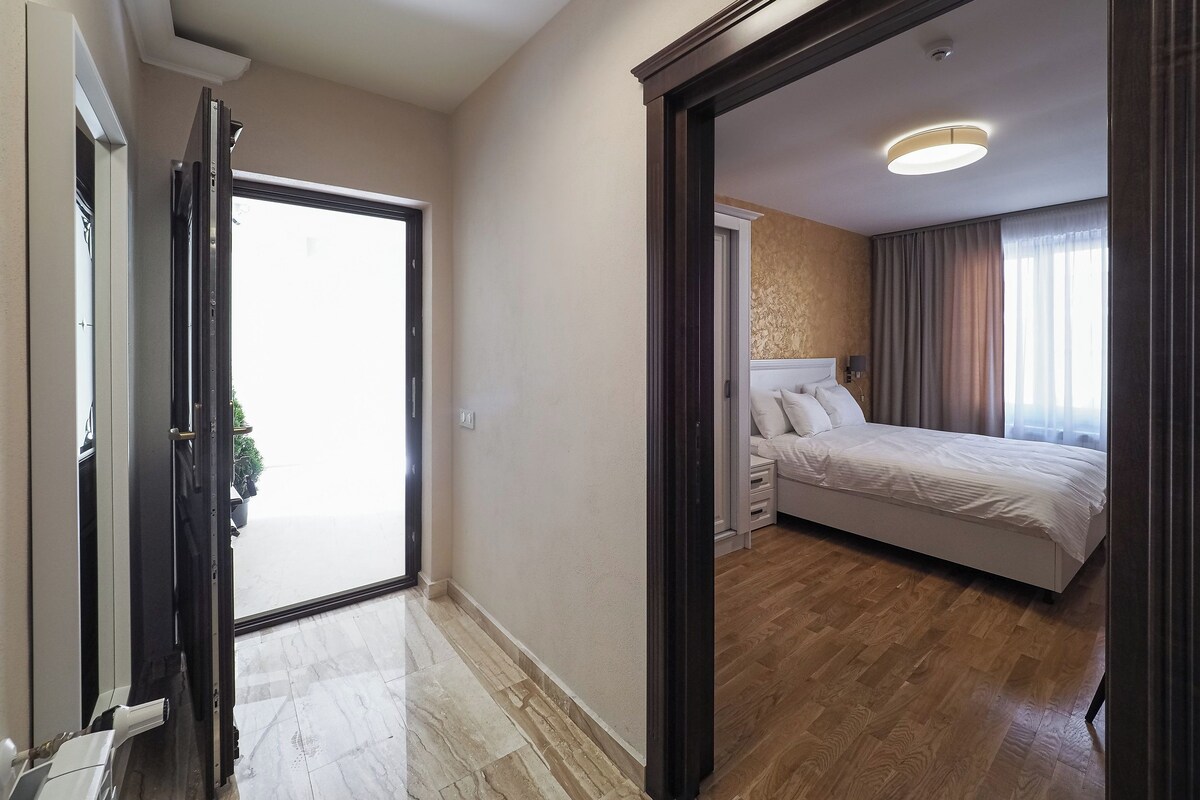 A hotel room with a bed, bedside table, and a view of the outside.