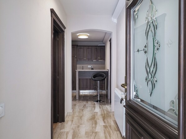 Un pasillo con una zona de cocina, un taburete de bar y una puerta de cristal decorativa.