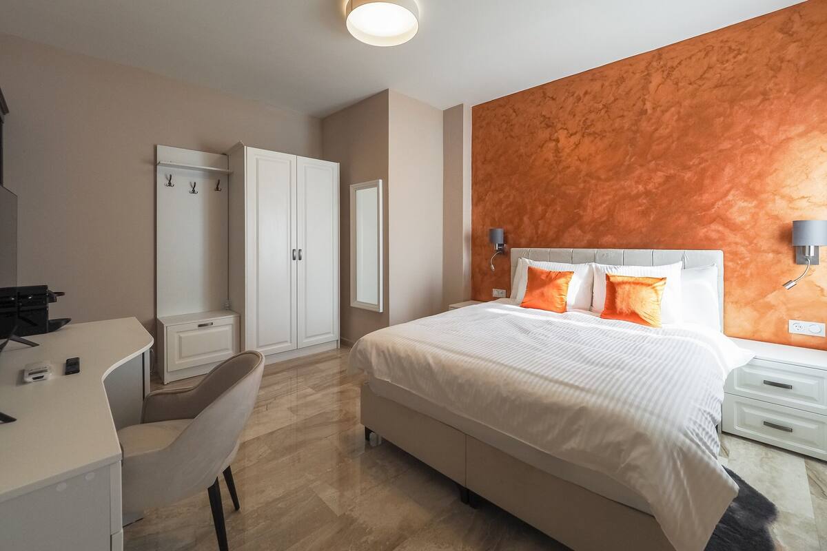 A hotel room with a bed, a desk, a chair, a wardrobe, and a wall-mounted lamp.