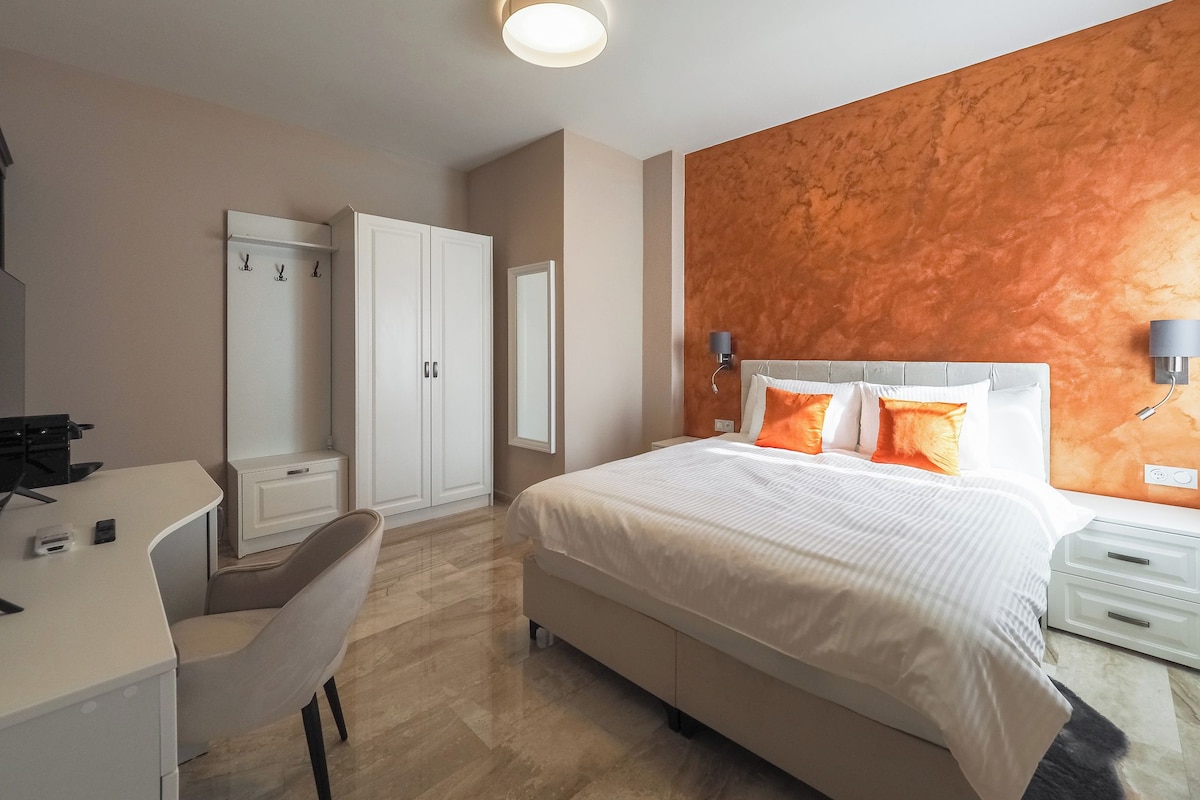 A hotel room with a bed, a desk, a chair, a wardrobe, and a wall-mounted lamp.