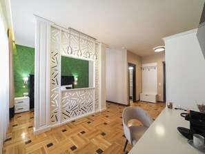 A modern living room with a herringbone wood floor, a grey upholstered armchair, a white coffee table, and a black coffee machine. - Boutique Central Sibiu (Sibiu)