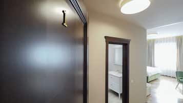 Habitación de hotel con un armario de madera, un espejo, una cama, una silla verde y un baño con un lavabo y mueble blancos.