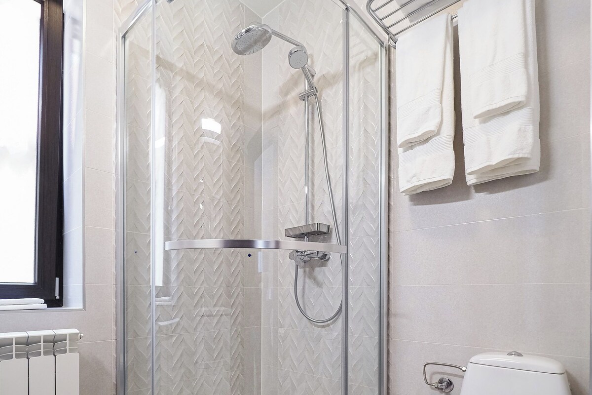Une salle de bain moderne dotée d’une douche à parois de verre, de toilettes et d’un porte-serviettes.