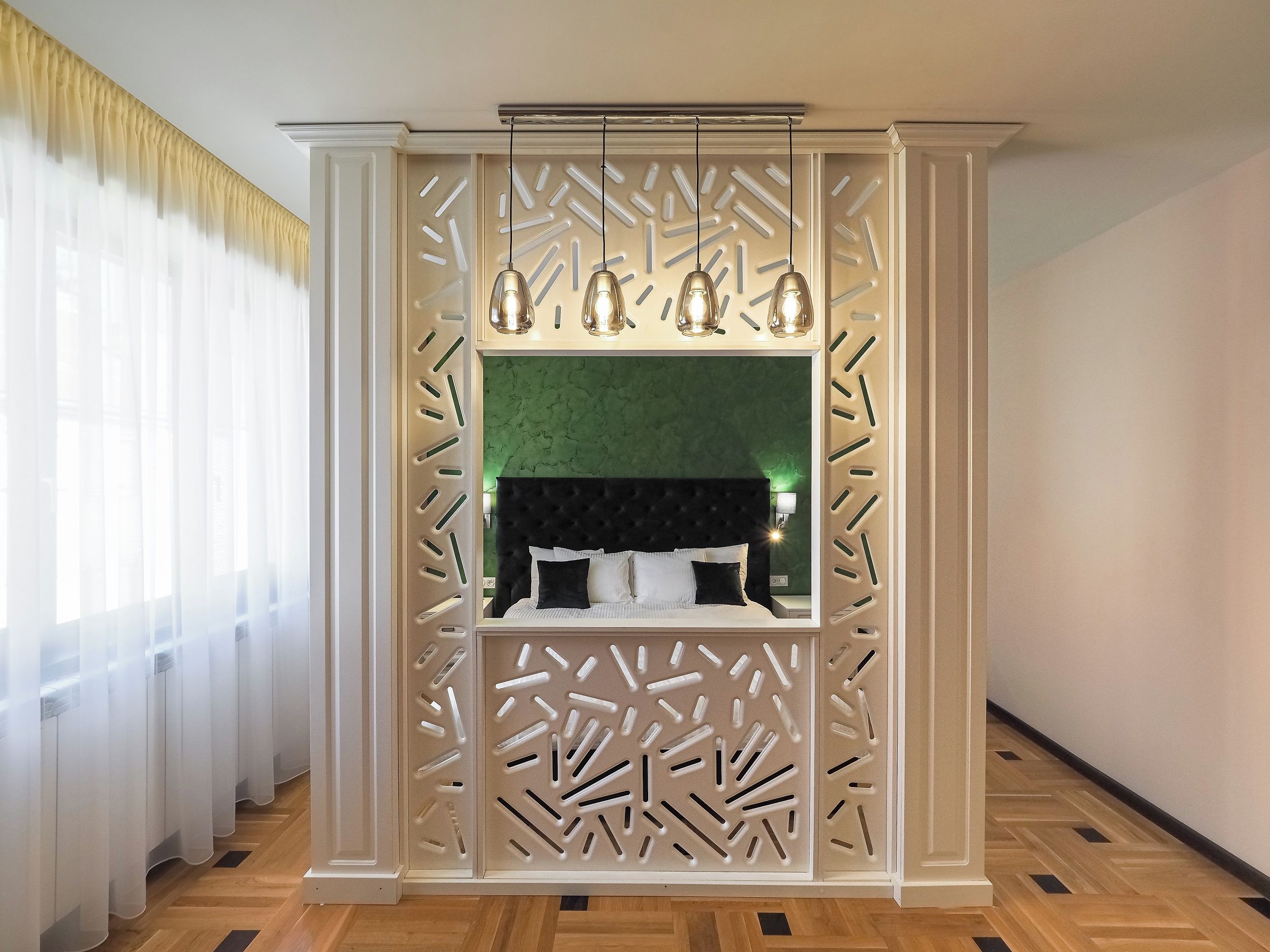 A bedroom with a green wall, a black headboard, and a decorative partition with light fixtures.