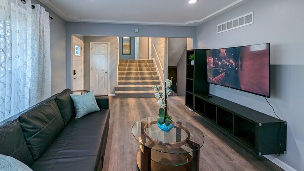 A living room with a sofa, a glass coffee table, a TV, and a staircase leading to another room. - Comfy, Spacious & Convinient 3/2 house in Overland Park (Overland Park)