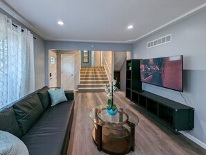 A living room with a sofa, a glass coffee table, a TV, and a staircase leading to another room.