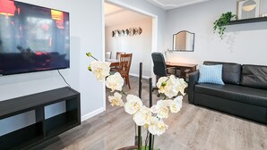 A modern living room with a flat-screen TV, a dining area with a table and chairs, a black sofa, and a potted orchid. - Comfy, Spacious & Convinient 3/2 house in Overland Park (Overland Park)