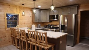 A modern kitchen with wooden bar stools, stainless steel appliances, and pendant lighting. - Newly Built Home: Perfectly Located Near Loon Mountain & Downtown Lincoln, NH! (Lincoln)