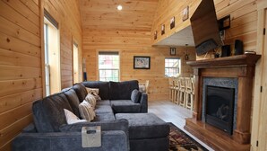 A cozy log cabin interior with a sectional sofa, a fireplace, and wooden walls. - Newly Built Home: Perfectly Located Near Loon Mountain & Downtown Lincoln, NH! (Lincoln)