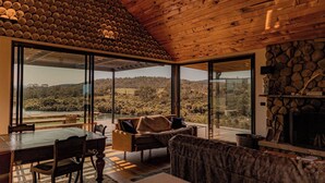 Um quarto espaçoso com uma grande mesa de jantar, um sofá e uma lareira. O quarto possui janelas amplas que oferecem vista para o exterior.