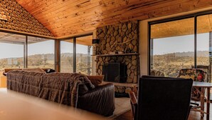 Quarto com uma cama grande, parede de pedra, lareira e vista para a paisagem.