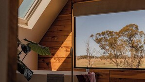Quarto com uma grande janela que oferece vista para árvores e um céu claro.