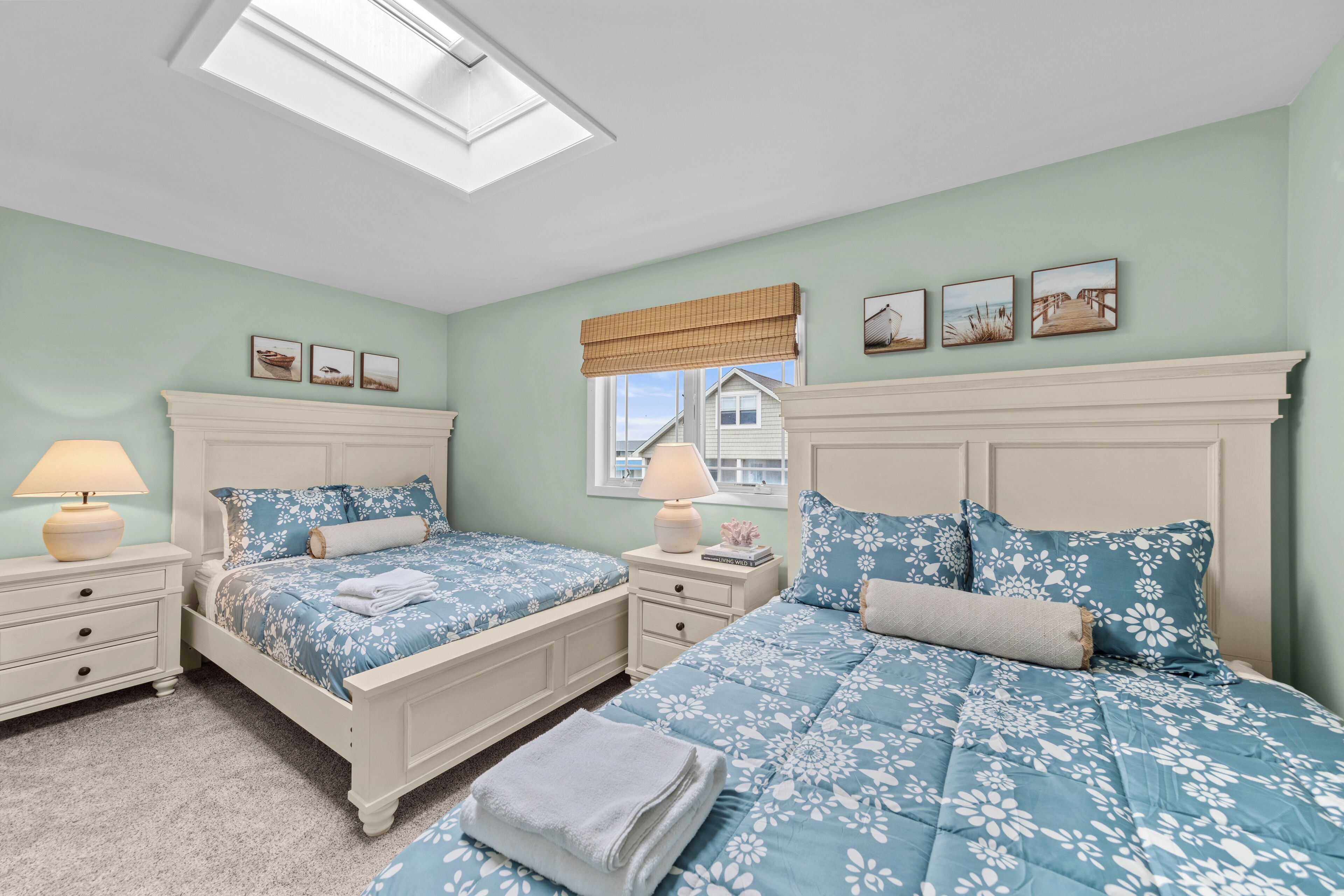 A bedroom with two beds, a skylight, a window with a view, and a set of framed pictures on the wall.