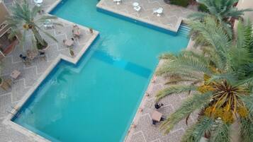A large rectangular pool with a tiled deck surrounding it, featuring several white tables and chairs.