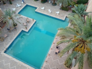 A large rectangular pool with a tiled deck surrounding it, featuring several white tables and chairs.