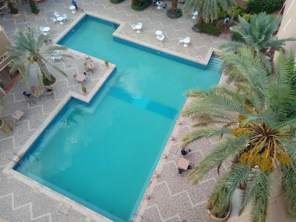 A large rectangular pool with a tiled deck surrounding it, featuring several white tables and chairs. - Le Tinsouline (Zagora)
