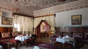 Una habitación tradicional con elaborados diseños en el techo, un comedor con mesas y sillas, y un conjunto de sofás.