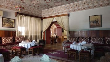A traditional room with ornate ceiling patterns, a dining area with tables and chairs, and a sofa set.