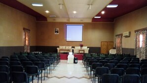 Un salón de conferencias con filas de sillas mirando hacia un atril y una pantalla.