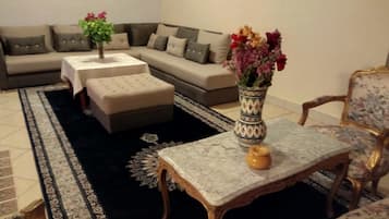 Una sala de estar con un sofá modular, un reposapiés, una mesita con un jarrón y una alfombra estampada.