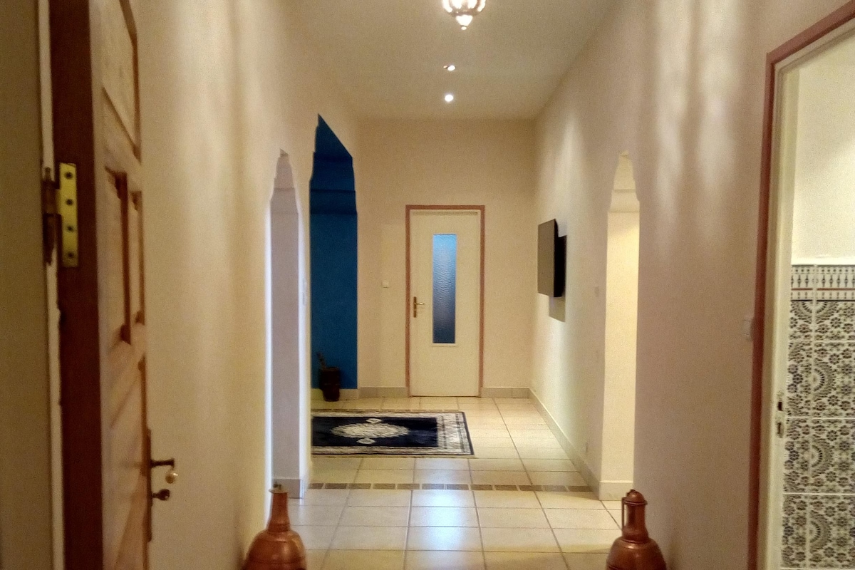 A hallway with a patterned rug, two vases, a chandelier, and a door with a blue accent.