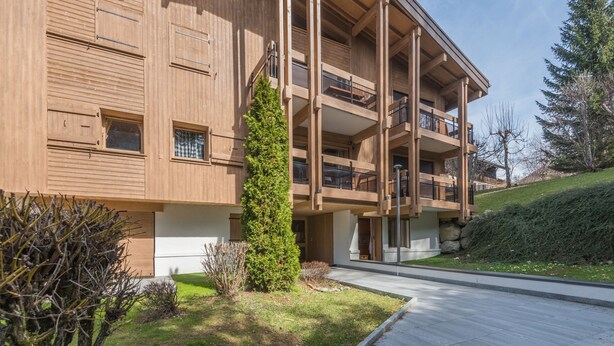 A modern multi-story building with balconies, a well-maintained lawn, and a clear sky.