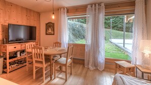 A wooden interior with a TV, dining table, chairs, and a window with curtains.