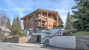 A multi-story wooden building with balconies, a stone wall, and a staircase leading to the entrance.
