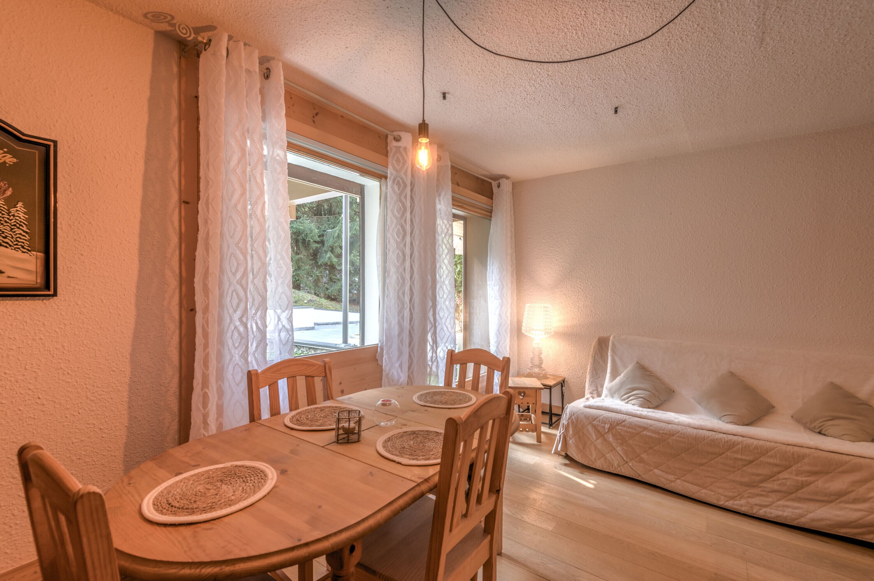 A cozy room with a wooden dining table, chairs, a bed with pillows, and a lamp.