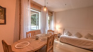 A cozy room with a wooden dining table, chairs, a bed with pillows, and a lamp.