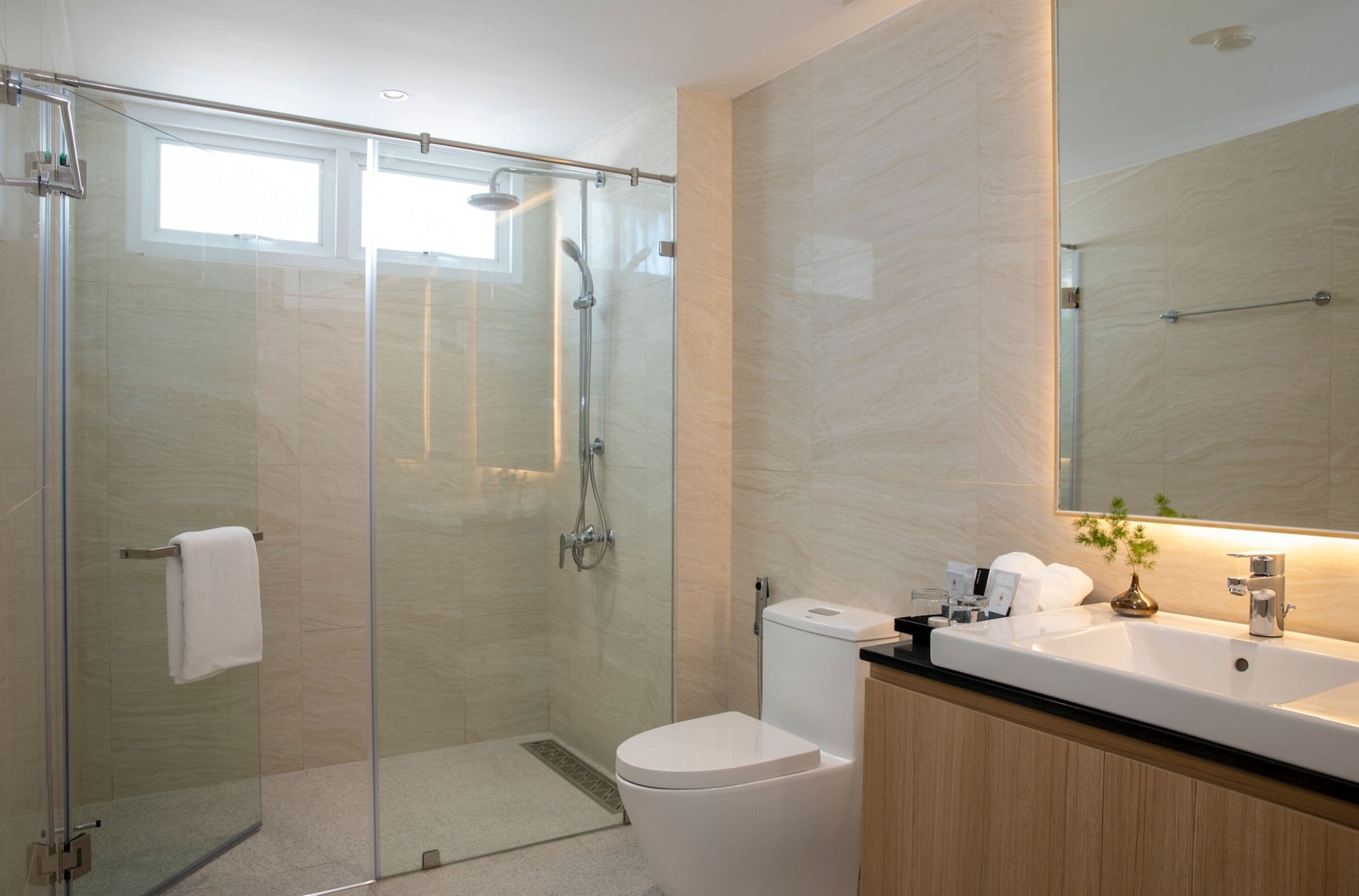 A modern bathroom with a glass-enclosed shower, a white toilet, and a large mirror above a sink with a wooden cabinet.