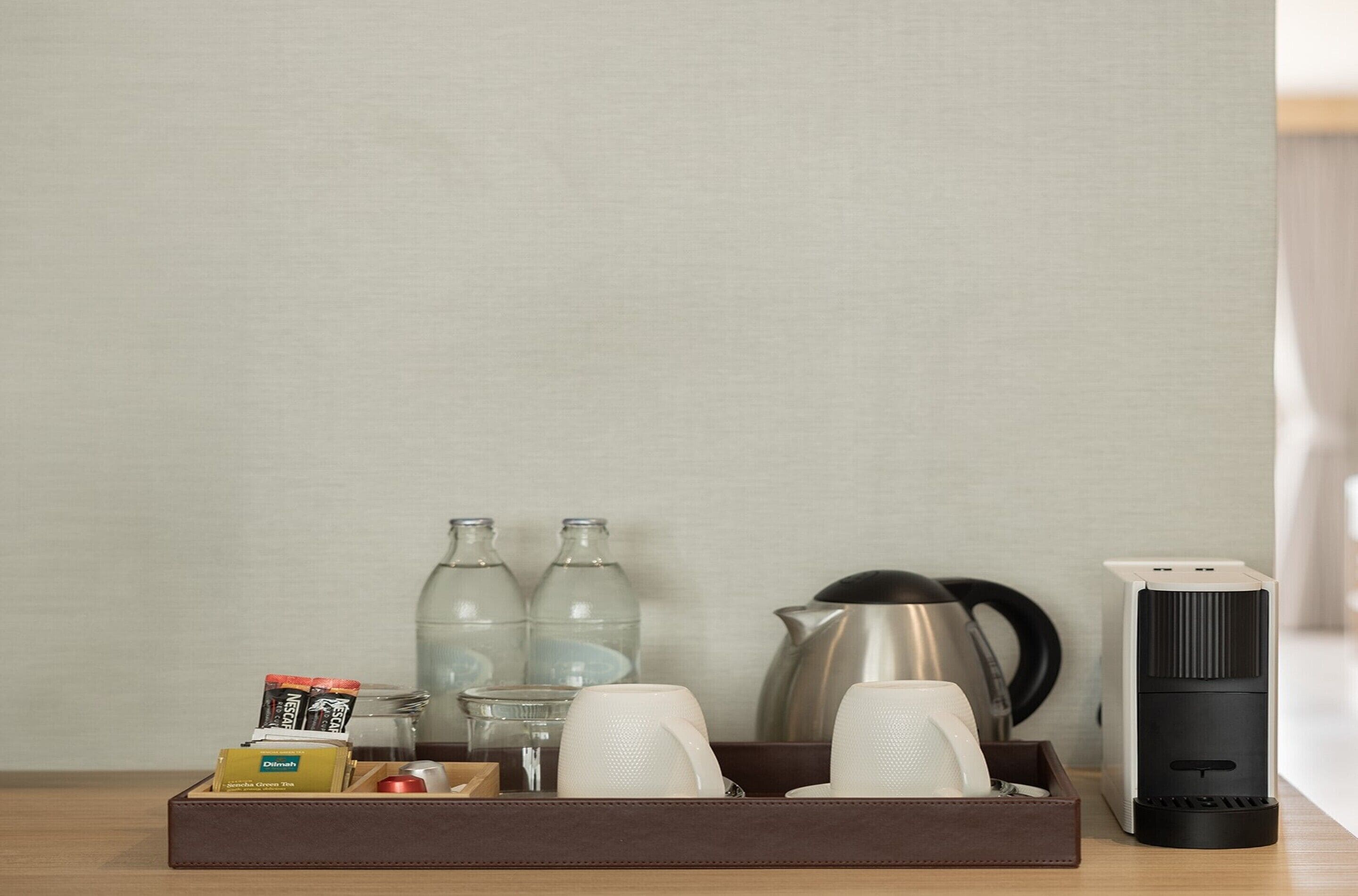 A neatly arranged tray with a coffee maker, two bottles, a kettle, and a box of tissues.