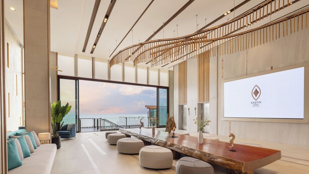 A modern hotel lobby with a large wooden reception desk, comfortable seating, and a large window offering a view of the sea. - Eastin Resort Rayong (Ban Chang)
