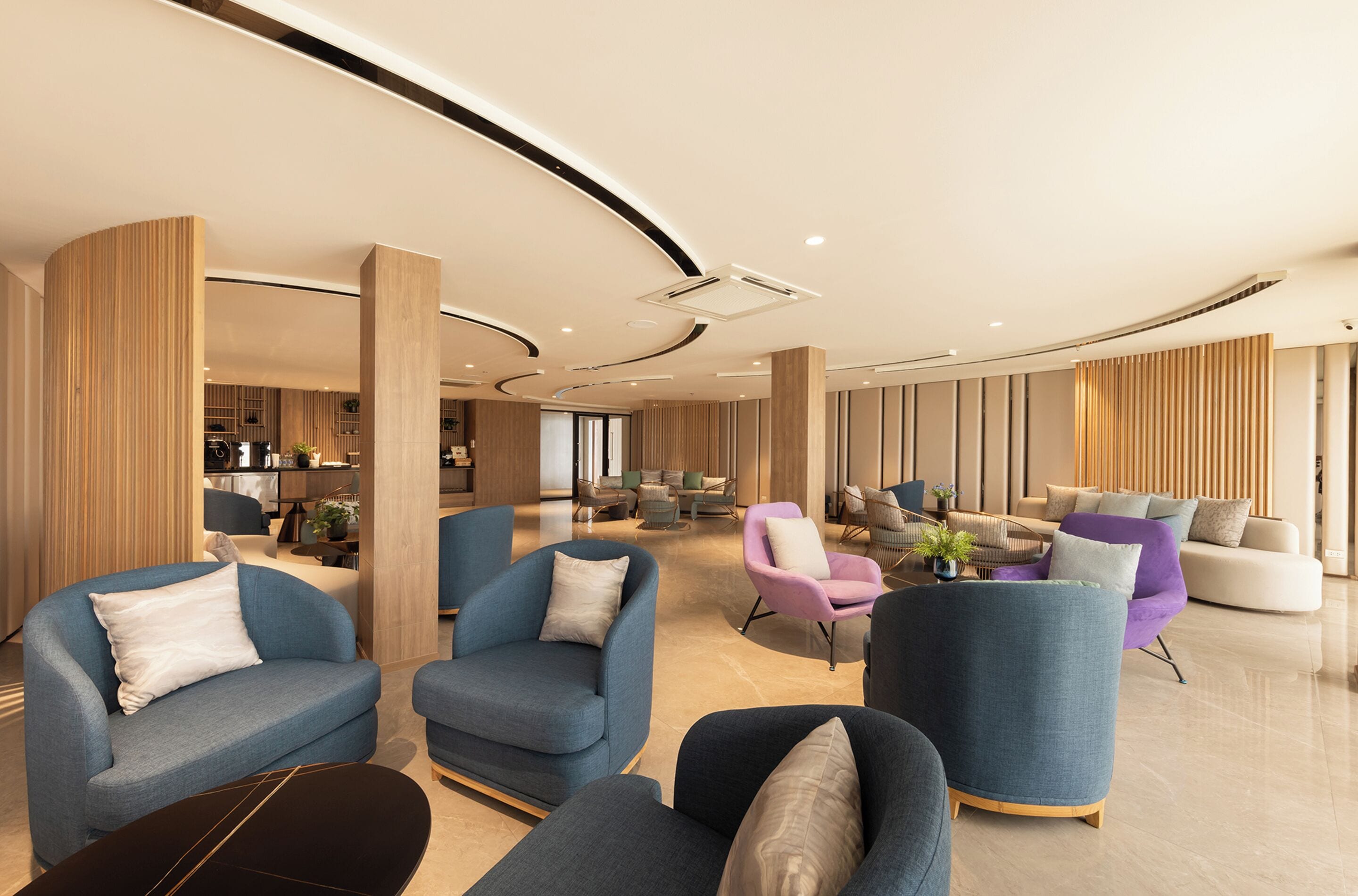 A spacious lobby with modern furniture, including sofas and armchairs, and a visible kitchen area in the background.