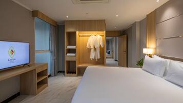 A modern hotel room with a large bed, a TV on a wooden stand, a wardrobe with hanging robes, and a mirror.