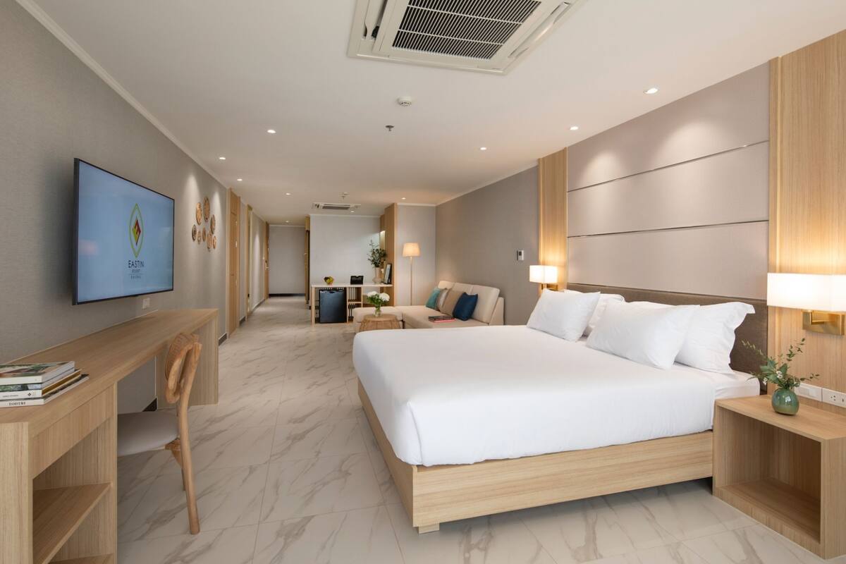 A modern hotel room with a large bed, a desk, and a television on the wall.